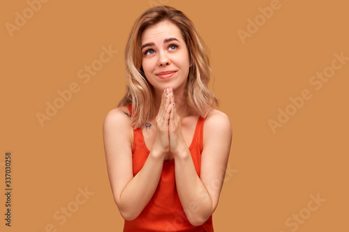 Photo Wishful female looks up, keeps palms together, begs for good luck