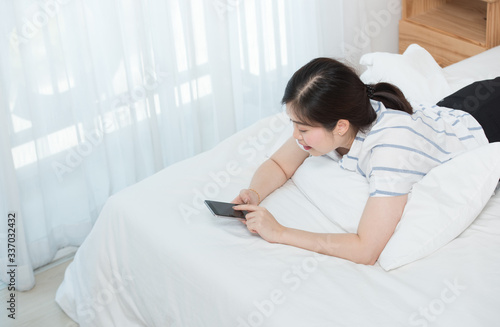 Rare view or back side of asian woman lay down on bed, holding smart phone and looking up thing something, no place like home.