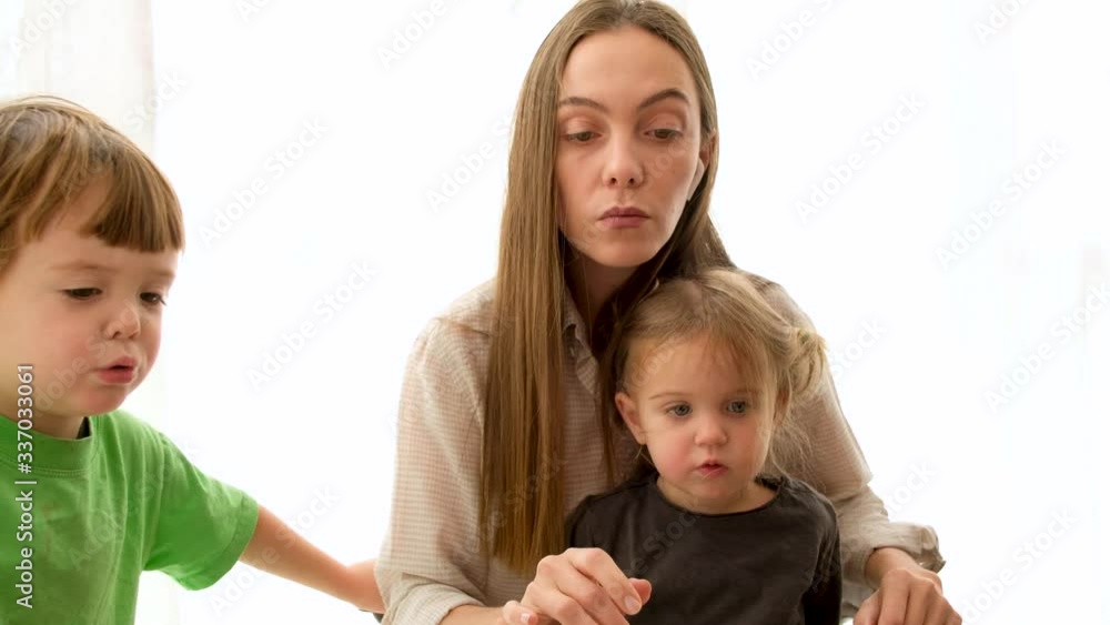 Tired adult mother hugging upset son and cute daughter and reaching out camera while taking care of children and working from home Tired adult mother hugging upset son and cute daughter and reaching out camera while taking care of children and working from home