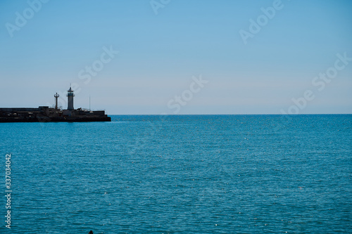 Lighthouse on the background of the sea and the sky  the sea is full calm and clear clear sky  spring. Lighthouse  sea and pier.