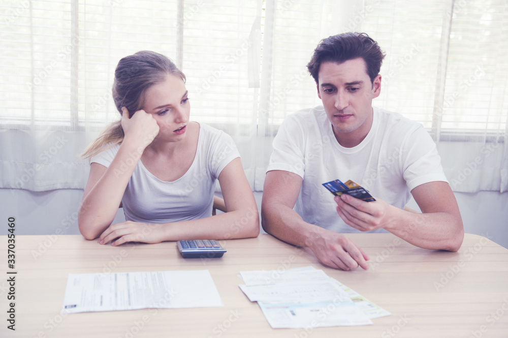 Young caucasian couple hand holding credit card and debt bill on table in home,men and women have overdue financial foreclosure problem sit in room with serious and unhappy payment. Young caucasian couple hand holding credit card and debt bill on table in home,men and women have overdue financial foreclosure problem sit in room with serious and unhappy payment.