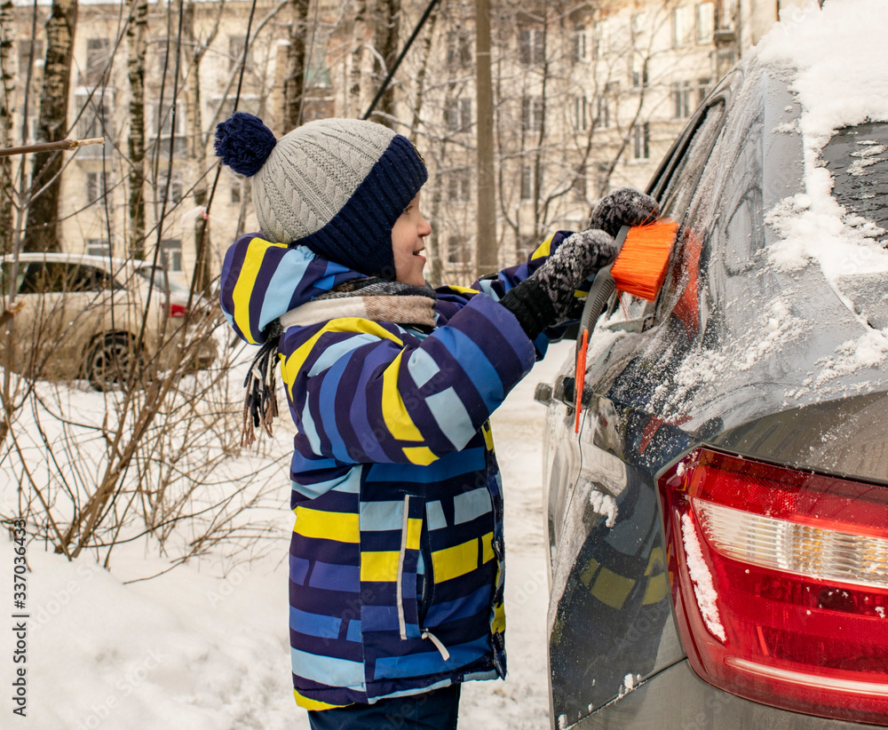 Fototapeta premium A little boy is happy to clear the car of snow.