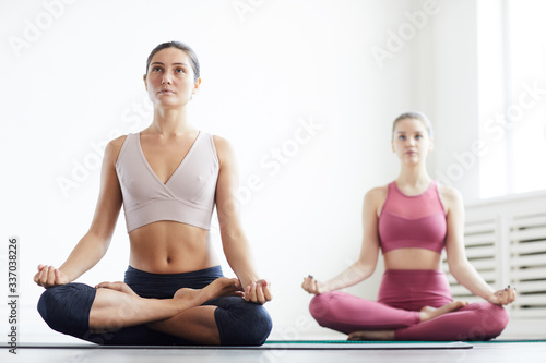 Portrait of two young women sitting in lotus position and doing yoga in class