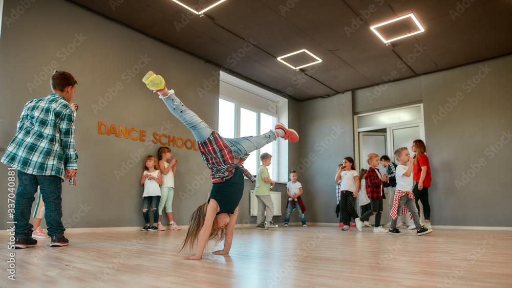 Fototapeta premium Breakdance. Full length portrait of a little girl standing on her hands while having a choreography class in the dance studio