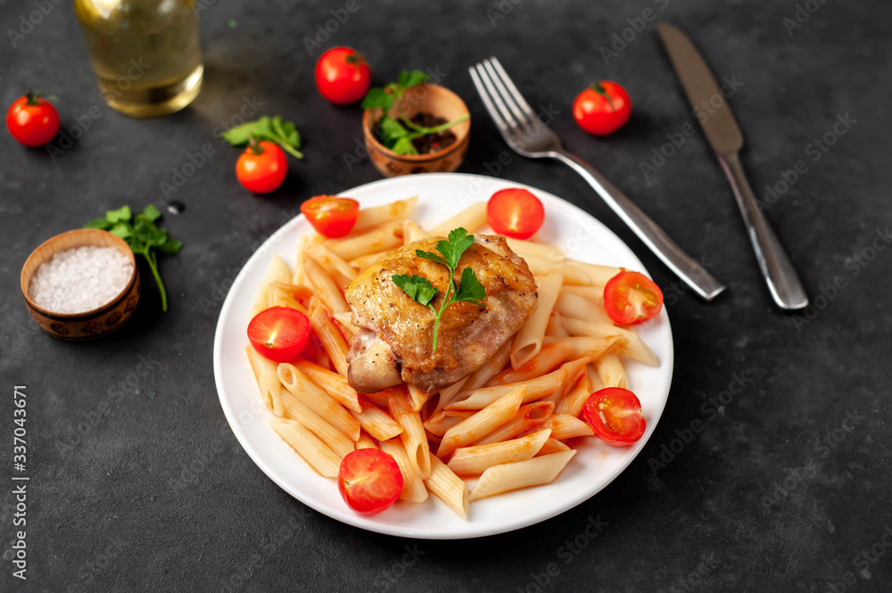 Penne pasta in tomato sauce with tomatoes and grilled chicken thigh in a white plate on a stone background Penne pasta in tomato sauce with tomatoes and grilled chicken thigh in a white plate on a stone background