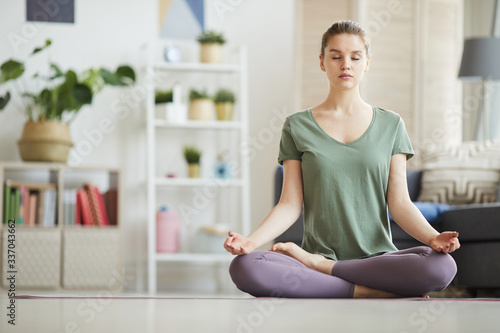 Portrait of healthy young woman sitting on the floor with her eyes closed and meditating at home