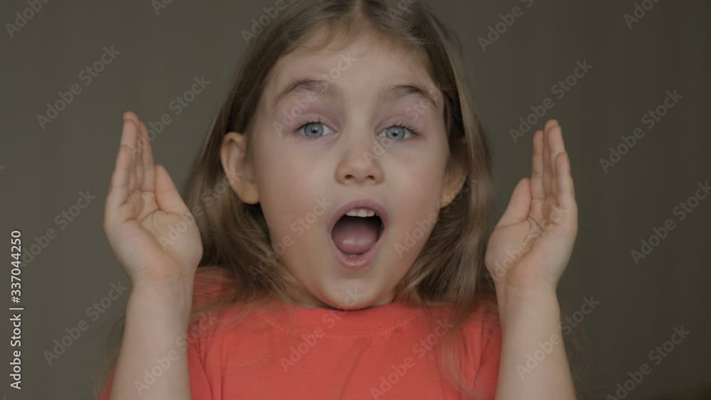 Cute little girl open her face with hands. Girl looks and is surprised and happy to receive a surprise. Portrait little young girl with blue eyes looking at camera. Closeup Cute little girl open her face with hands. Girl looks and is surprised and happy to receive a surprise. Portrait little young girl with blue eyes looking at camera. Closeup