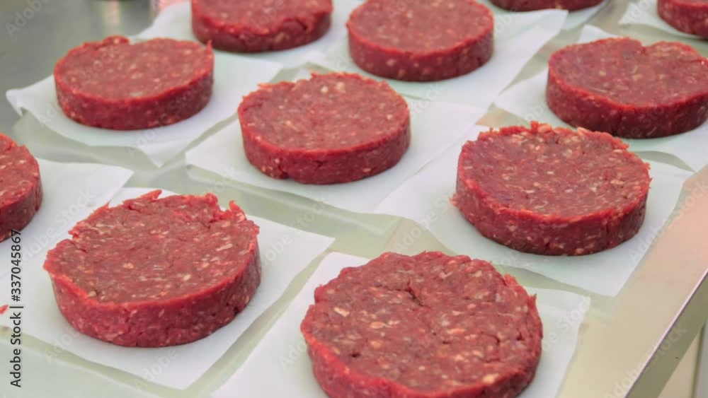 Many raw hamburgers sitting on interleaver papers on top of a stainless steel stand Many raw hamburgers sitting on interleaver papers on top of a stainless steel stand