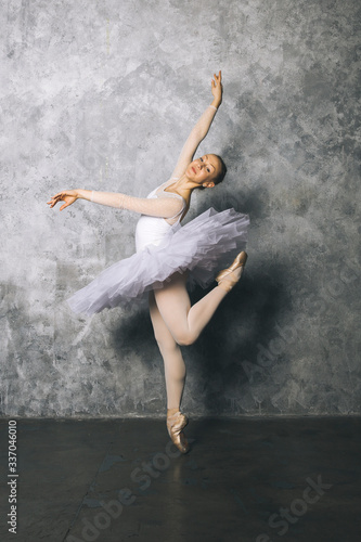 Pretty young ballerina dancer dancing classical ballet against rustic wall