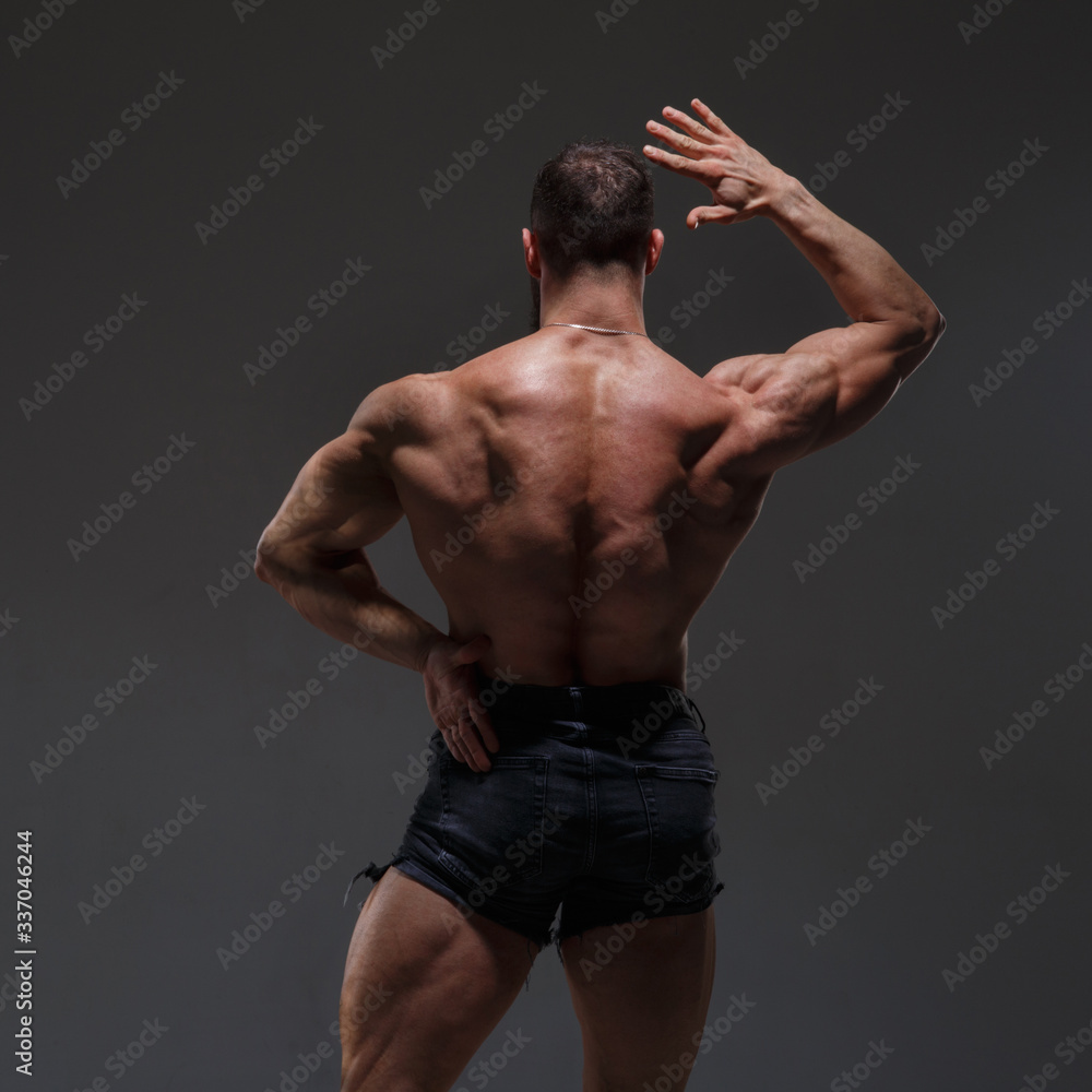 Portrait of a  athletic man with a naked torso showing muscles isolated on a dark gray background, view from the back.