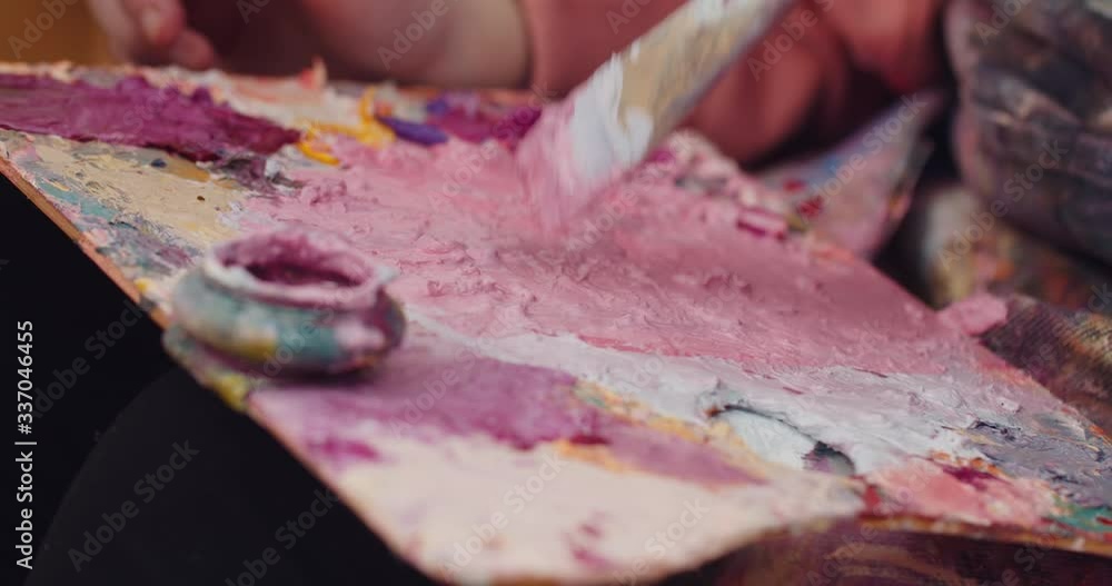 Close up view of artist palette with pink, yellow, white and purple colours on it. Art palette with mixed spots and brush soaking into paint . Concept of creativity and picture painting. Close up view of artist palette with pink, yellow, white and purple colours on it. Art palette with mixed spots and brush soaking into paint . Concept of creativity and picture painting.