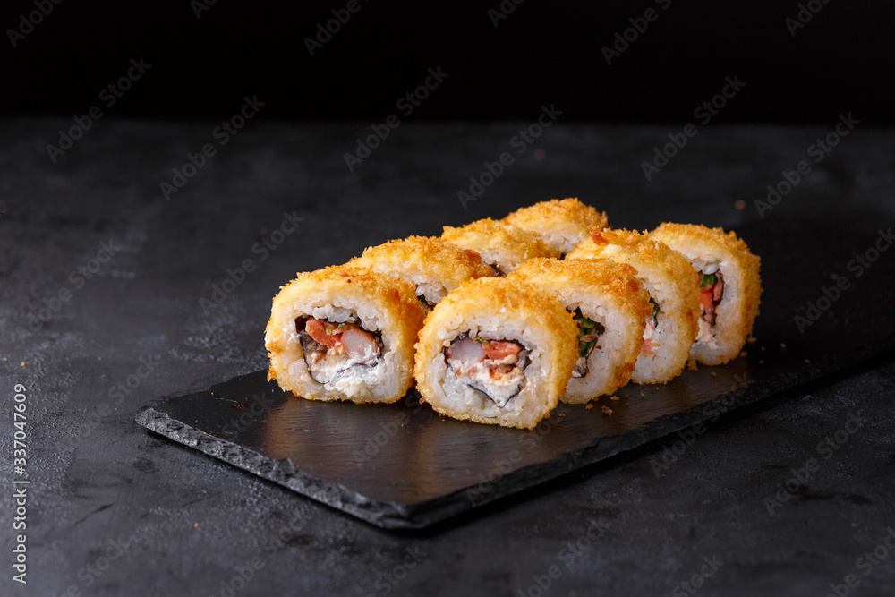 Sushi rolls with salmon, eel, shrimp, nori, cremette cheese, cucumber on a black background.