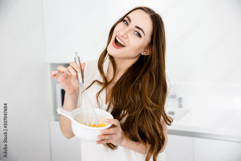 Happy Girl of European Appearance Beats Eggs for Breakfast on an Abel Background and Looks at the Camera Happy Girl of European Appearance Beats Eggs for Breakfast on an Abel Background and Looks at the Camera