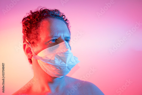 man with face mask lit laterally by red and blue lights looking to the right