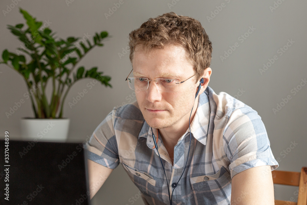 Programmer in headphones working from home, remote, home office. A man with glasses looks at the monitor. Remote work concept Programmer in headphones working from home, remote, home office. A man with glasses looks at the monitor. Remote work concept