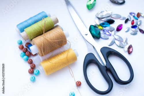 Accessories for needlework thread, beads, rhinestones, scissors on a white background, soft focus