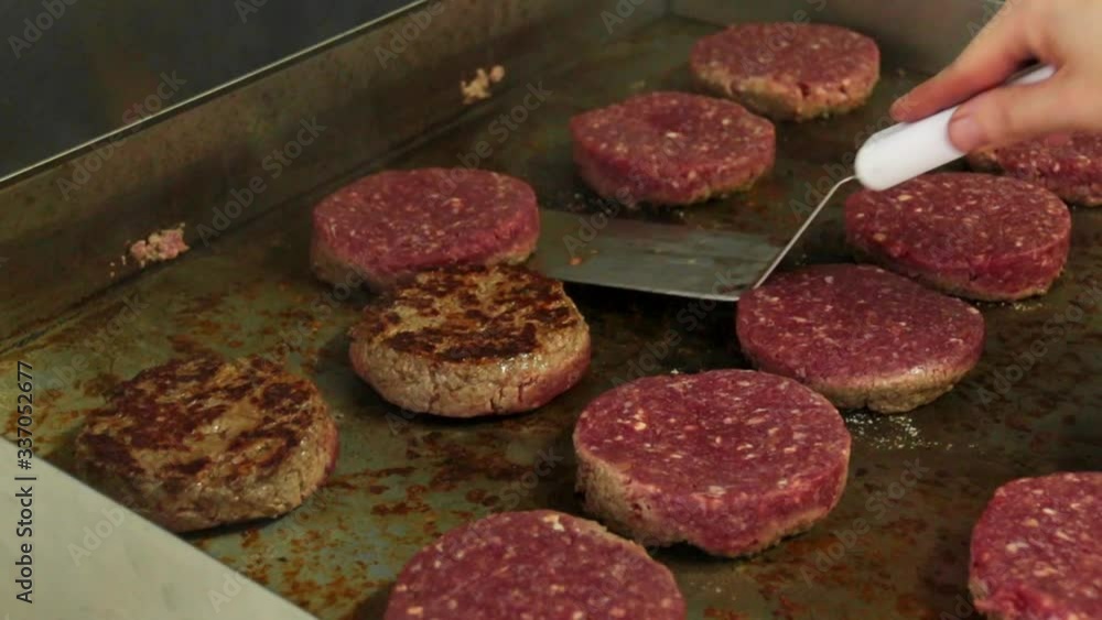 Chef flipping hamburger patties with a spatula on a griddle Chef flipping hamburger patties with a spatula on a griddle