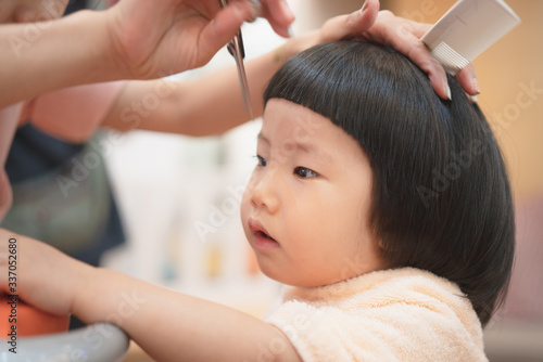 Portrait of cute Asian toddler girl had a hair cut by mother during the Covid-19 coronavirus pandemic, DIY, self-quarantine, social distancing, mother daughter relationship, trust, self haircut, trust
