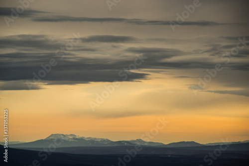 yellow sunset sky with large blue clouds against the background of mountains