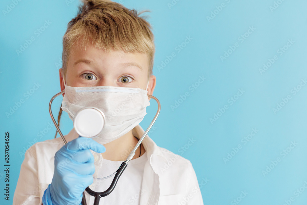 A little boy plays doctor, a concept of choosing a profession for a child, a blond boy in a white shirt, wearing a protective face mask and with a phonendoscope A little boy plays doctor, a concept of choosing a profession for a child, a blond boy in a white shirt, wearing a protective face mask and with a phonendoscope