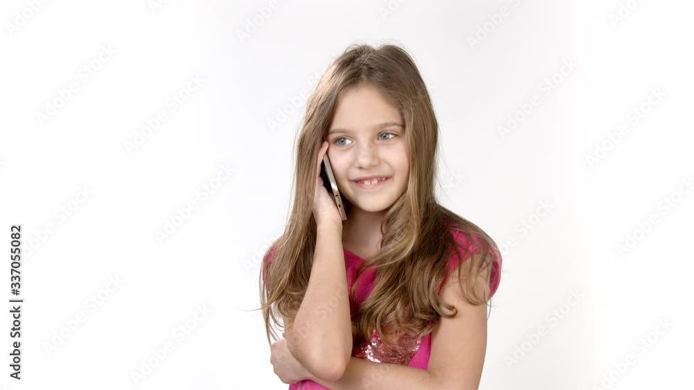 Emotional conversation on the phone of a little girl. A little girl is on the phone in a bright pink dress on a white background Emotional conversation on the phone of a little girl. A little girl is on the phone in a bright pink dress on a white background