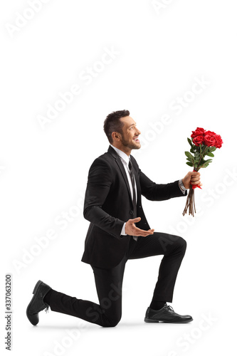 Young handsome man kneeling with a bunch of red roses photo