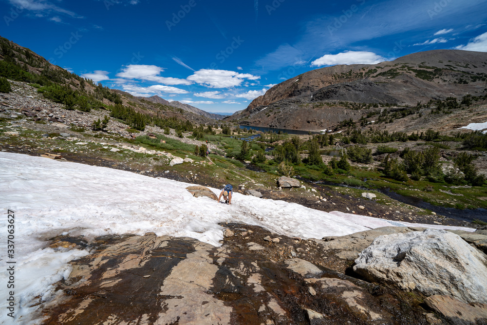 Female hiker looking distressed struggles to climb up a steep mall snow field in the Eastern Sierra California, 20 Lakes Basin hike