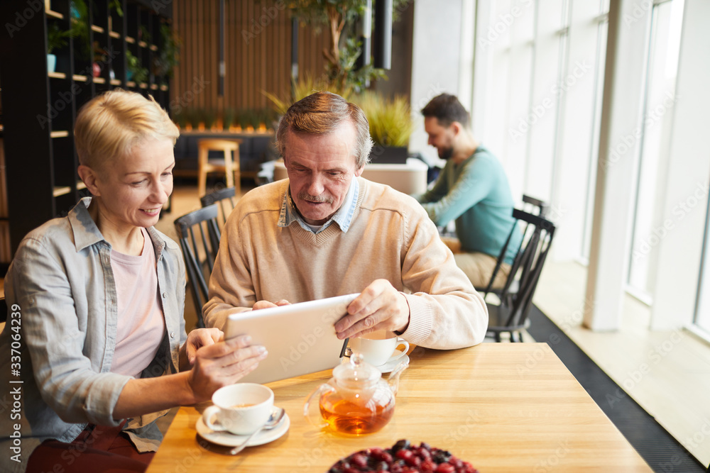 Mature couple using digital tablet while drinking tea at the table in the restaurant Mature couple using digital tablet while drinking tea at the table in the restaurant