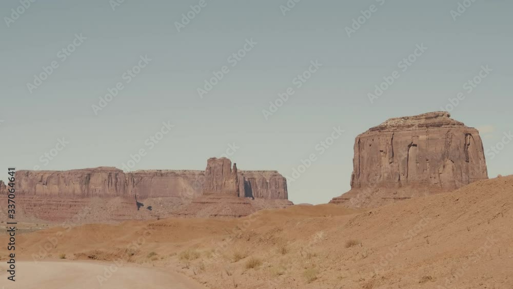 Driving On Dusty Dirt Road In Desert Among Red Rocks Buttes Of Monument Valley Driving On Dusty Dirt Road In Desert Among Red Rocks Buttes Of Monument Valley