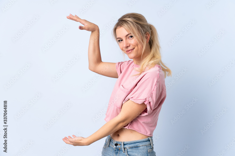 Blonde woman over isolated blue background holding copyspace to insert an ad Blonde woman over isolated blue background holding copyspace to insert an ad