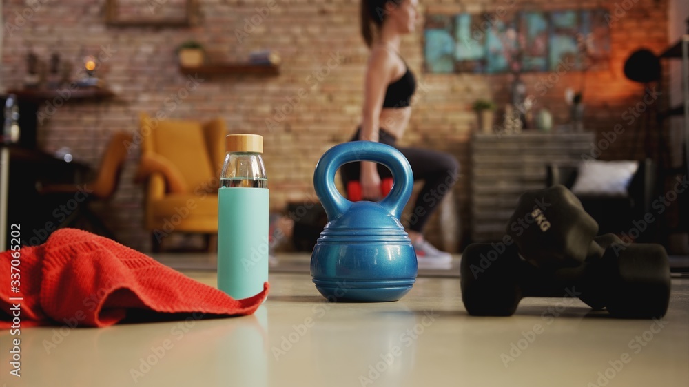 Fototapeta Fitness training at home. Young woman doing leg workout, exercising in living room. Focus on fitness equipment. Stay at home and stay fit and healthy.