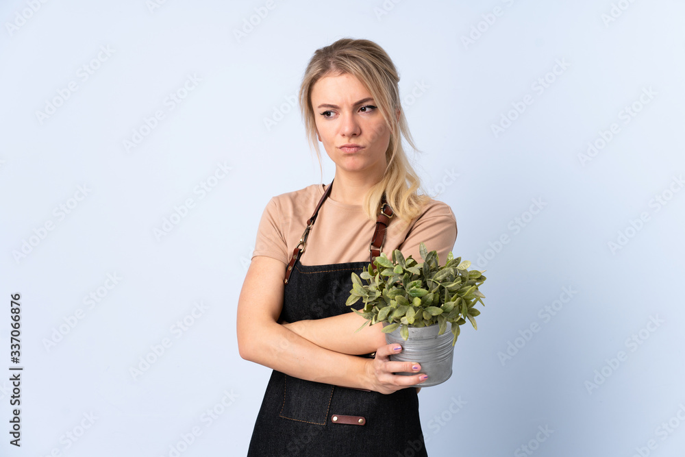 Blonde gardener woman holding a plant over isolated background thinking an idea Blonde gardener woman holding a plant over isolated background thinking an idea