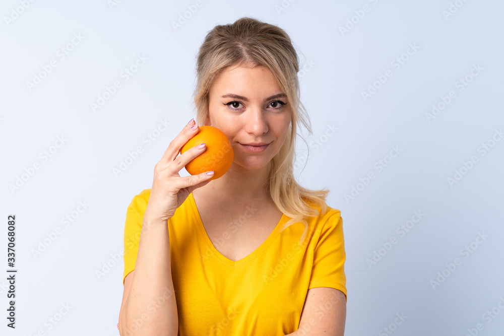 Blonde woman over isolated blue background holding an orange Blonde woman over isolated blue background holding an orange