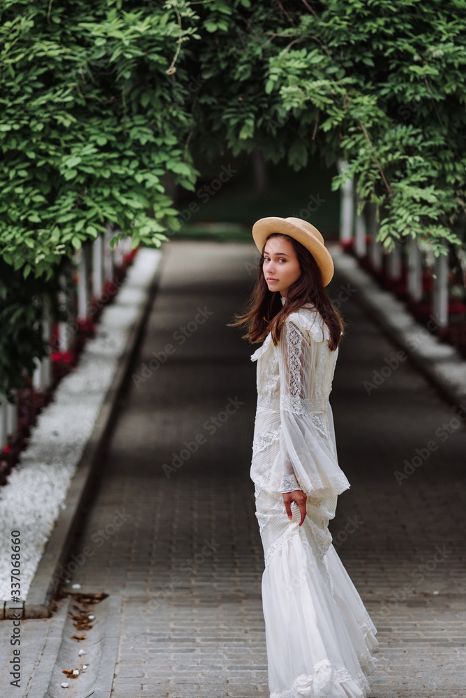 girl in a white dress and a straw hat walks in a beautiful park. bride in a vintage wedding dress in the garden.