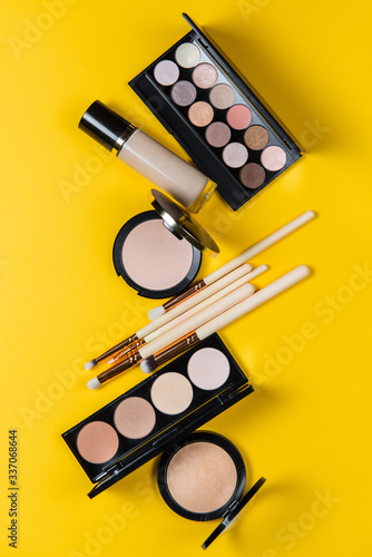 Makeup brushes, powder, eyeshadow palette, foundation for the face on a yellow background with place for text, top view