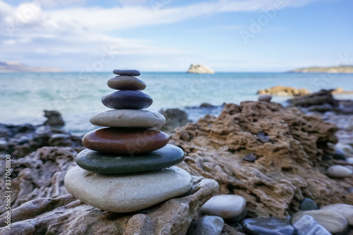 Pyramid of pebble stones on the sea beach. Concept of harmony and dzen in contrast to wavy sea and sharp rocks.