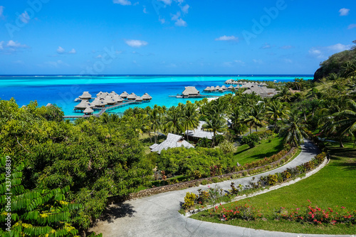Photo Overwater Bungalows in Turquoise Pacific Ocean Through Palms and Tropical Foliag