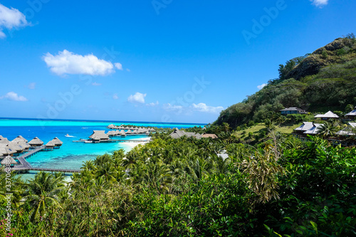 Fototapeta Naklejka Na Ścianę i Meble -  Overwater Bungalows in Turquoise Pacific Ocean Through Palms and Tropical Foliage in Bora Bora French Polynesia