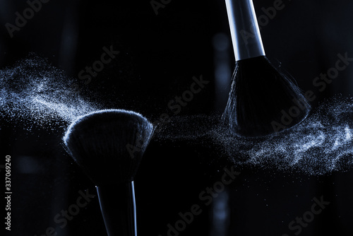 Powder in motion and makeup brushes close-up on a dark background