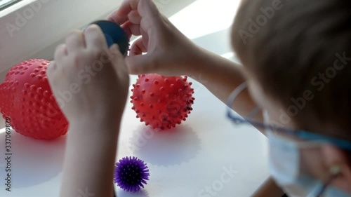 boy in opposite the window is standing, in a medical mask and glasses, boy in a medical mask listens to balloons with spikes with a medical stethoscope listening to balls with spikes similar to virus photo