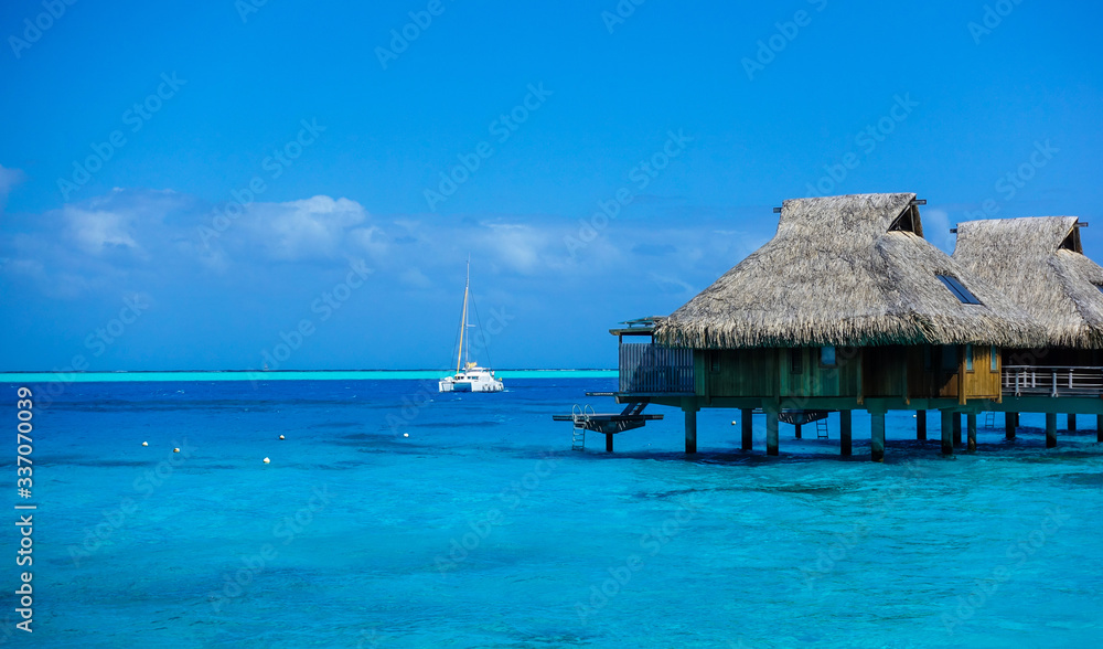 Overwater Bungalows over Blue Pacific Ocean with Catamaran Sailing in Bora Bora French Polynesia