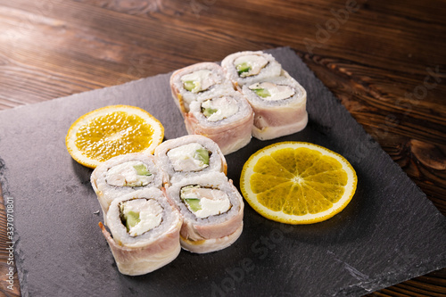 Sushi rolls with bacon, avocado and white fish with sliced orange on the black japan plate