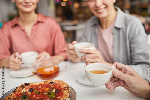 Close-up of family sitting at the table eating pizza and drinking tea together in cafe