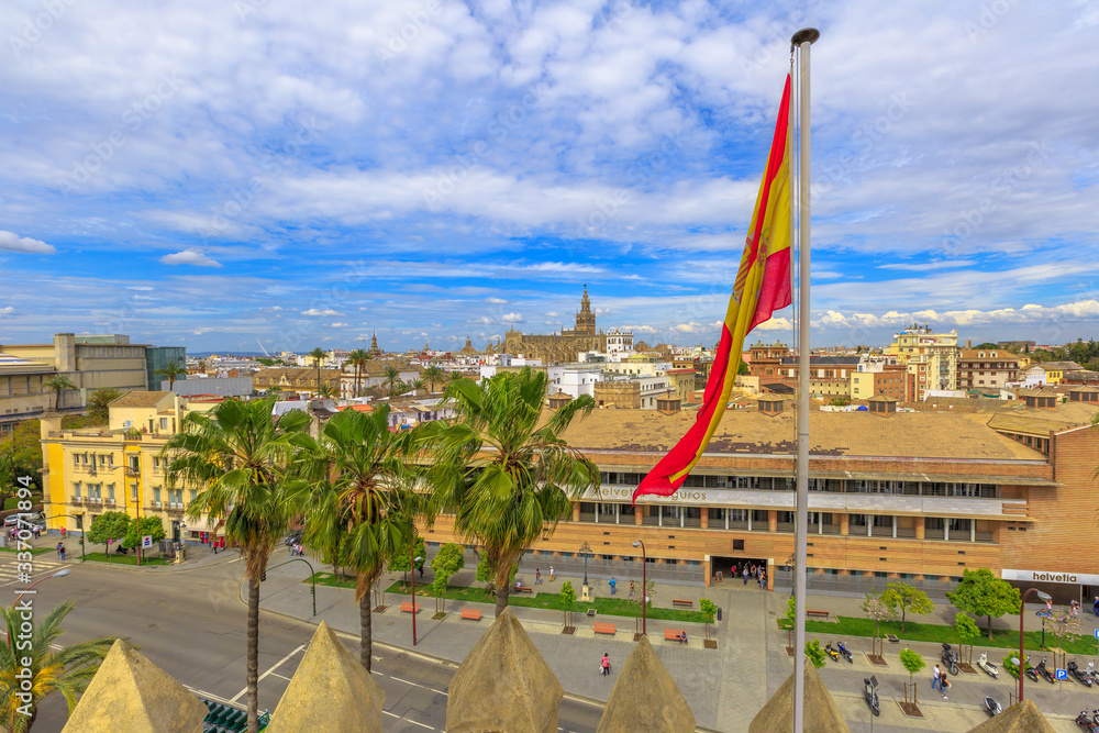 Aerial view of Seville skyline with Spanish flag in foreground. In the distance, the famous Seville Cathedral of Saint Mary of the See. Andalusia, Spain.