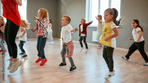 Full of energy. Group of little boys and girls dancing while having choreography class in the dance studio. Female dance teacher and children