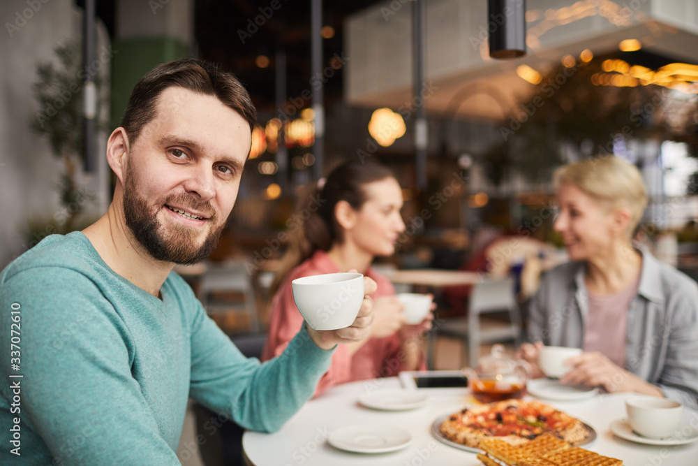 Portrait of young man smiling at camera and drinking tea with his family during lunch Portrait of young man smiling at camera and drinking tea with his family during lunch