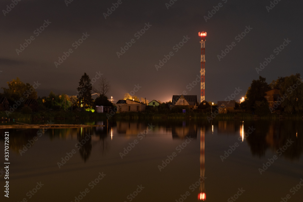 
Night city landscape with a pond and a cell tower