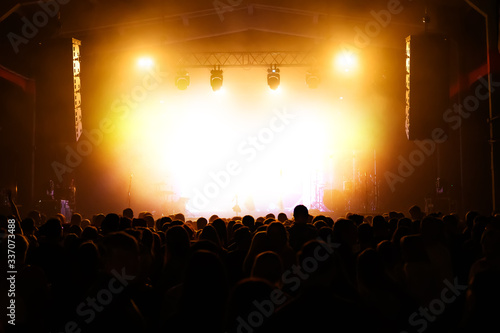 crowd at a concert festival awaiting an artist on stage. banner for a music show. illuminated stage and backs of people