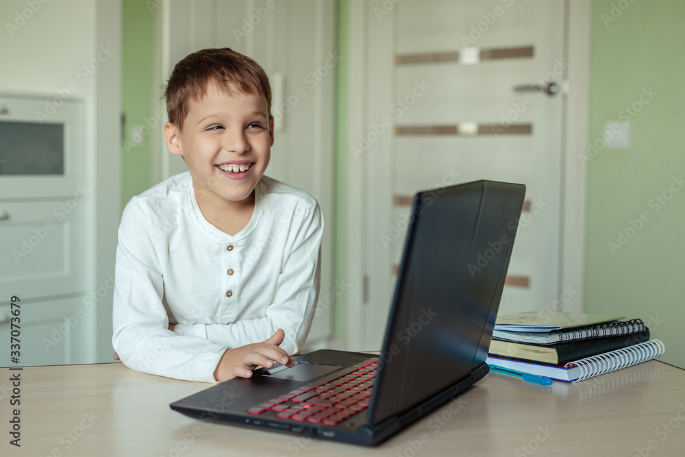Fototapeta premium home electronic distance learning. Cute happy child doing homework at home using a laptop. covid-19 epidemic and pandemic education