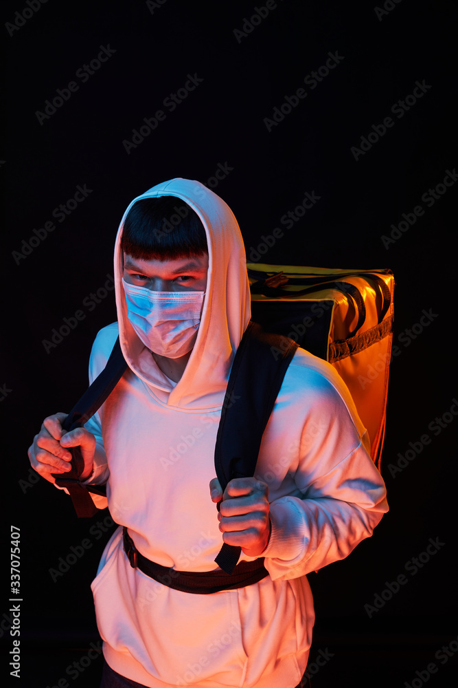 delivery man in white clothes in medicine mask with a yellow backpack on a black background